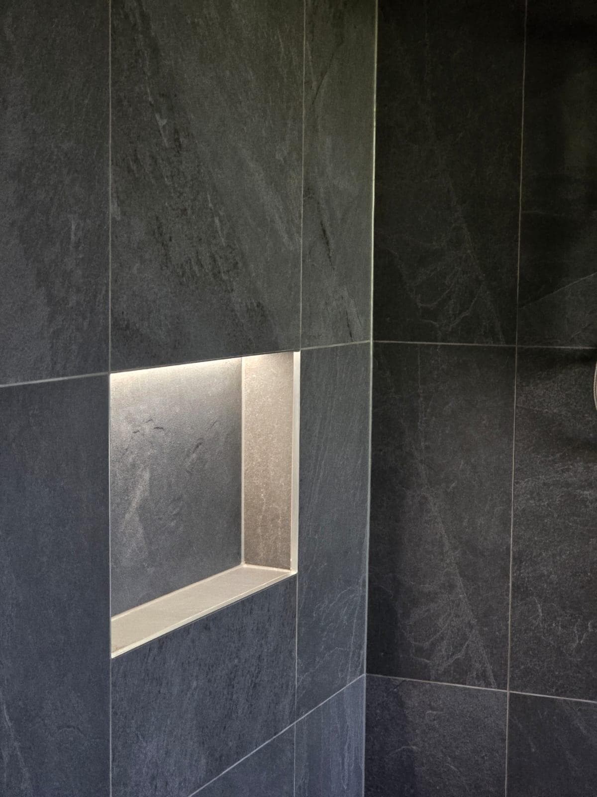 Modern bathroom renovation in Canberra with dark slate tiles and illuminated niche.