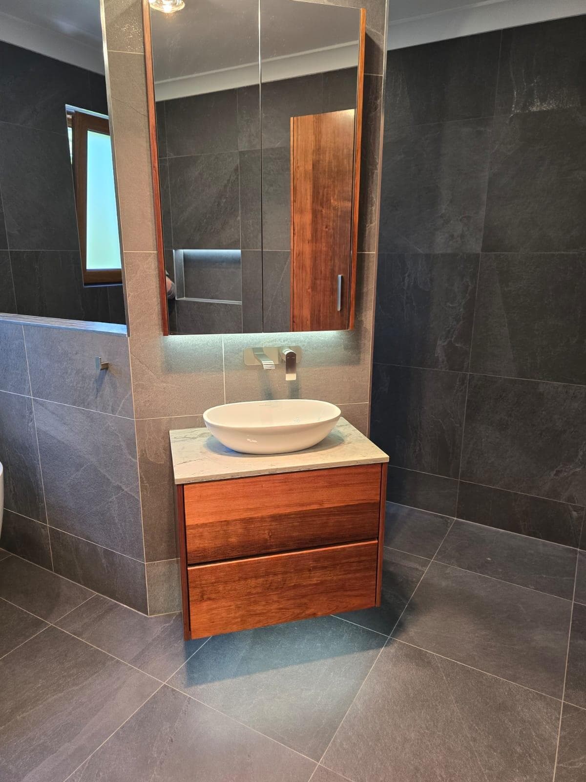 Modern bathroom renovation in Canberra with dark tiles and timber vanity