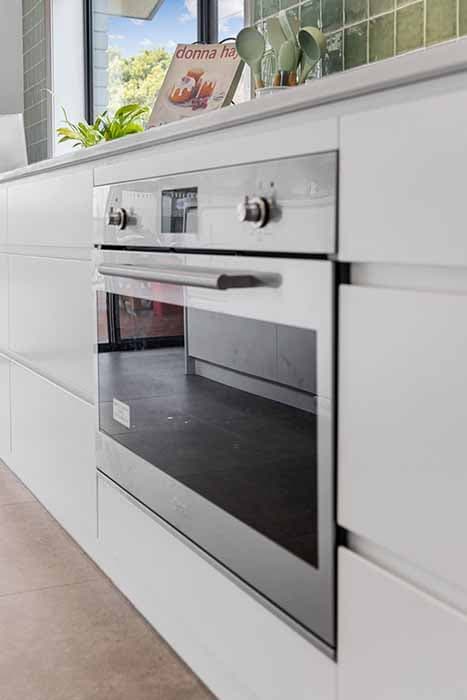 Modern kitchen renovation in Canberra, Australia with sleek cabinetry and green tile backsplash.