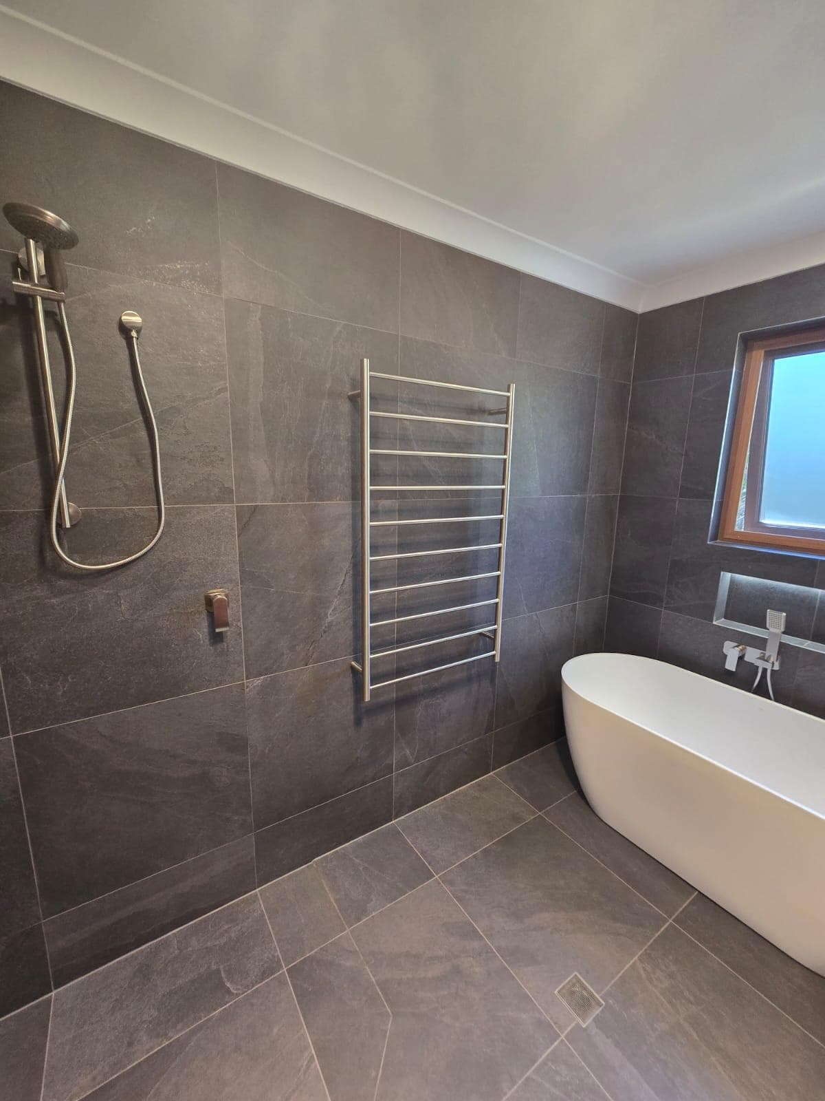 Modern bathroom renovation in Canberra with freestanding tub and dark tiles