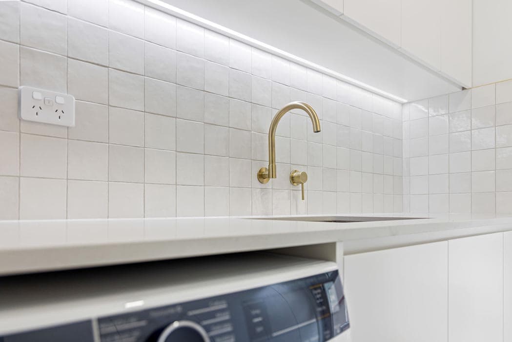 Modern laundry renovation in Canberra, Australia with stylish gold fixtures and white tiles.